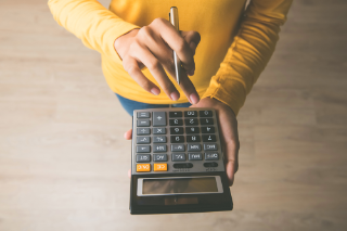 Woman entrepreneur using a calculator with a pen in her hand, calculating financial expense at home office