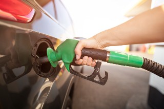Closeup of man pumping gasoline fuel in car at gas station. Gas pump nozzle in the fuel tank of a gray car