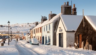 Helmsdale, Scotland, UK - December 2, 2010: A person walks their dog through winter snow on Shore Street in the village of Helmsdale in the Highlands of Scotland.