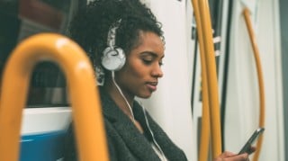 Young woman on a train listening to music on headphones and looking at her smartphone.