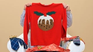 Man holding up a red jumper with a Christmas pudding on it in front of his face.