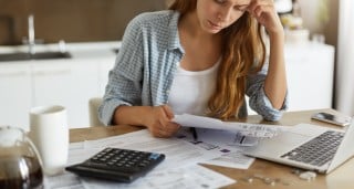 image of woman with laptop looking at bills and calculator 