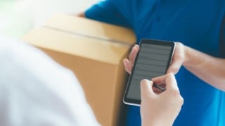 Close up of a man signing a device and taking delivery of a parcel from a delivery person.