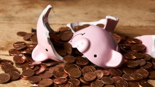 Smashed pink piggy bank upside down on top of a pile of copper coins, on a wooden table or floor.