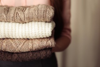 Close up photograph of someone holding a pile of four folded jumpers.