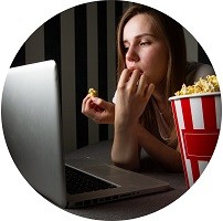 Teenage girl eating popcorn while watching something on a laptop.