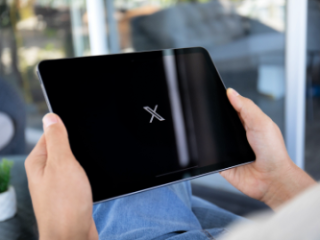 Close up photograph of a person opening X, formerly Twitter, on a tablet.