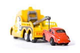 Photo of a yellow toy pick-up truck towing a red toy car.