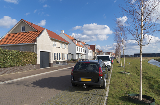 Cars parked on the side of the road opposite white buildings under a blue sky.