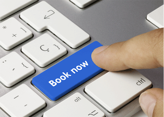Close up of a finger pressing a blue key marked 'Book now' on a keyboard.