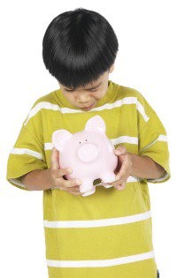 Young boy wearing a T-shirt holding a piggy bank and looking down at it.