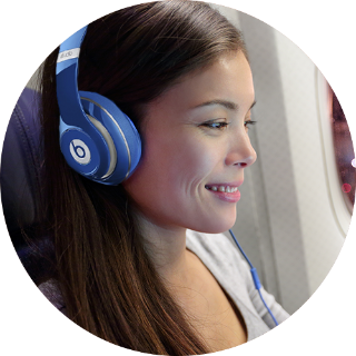 Young woman wearing blue Beats headphones smiling while sitting on an airplane.