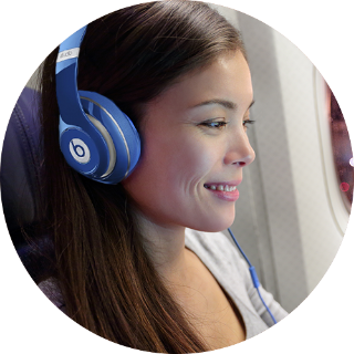 Young woman wearing blue Beats headphones smiling while sitting on an airplane.