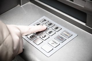 Close up of a hand entering a PIN into the keypad of an ATM.