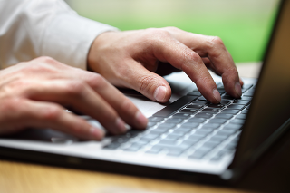 Close up on man's hands as he types on a laptop while sat at a table or desk.