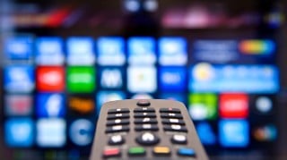 Close up of a television remote control pointing at a television screen in the background.