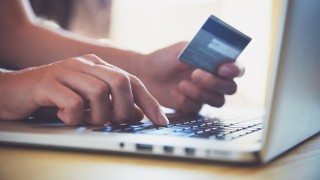 close up image of person typing on laptop computer with one hand and holding debit card in another