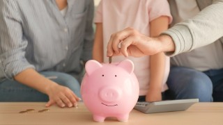 Little girl with her parents  putting coins into piggy bank indoors. Money savings concept