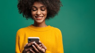 Portrait of a smiling young african woman wearing sweater standing isolated over green background, using mobile phone