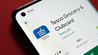 Tesco clubcard app seen in Google Play Store on the smartphone screen placed on red background. Close up photo with selective focus. Stafford, United Kingdom, August 2, 2022.