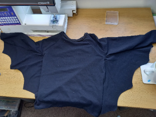 A black bat costume converted from a sweater. It lies on a table next to a sewing machine