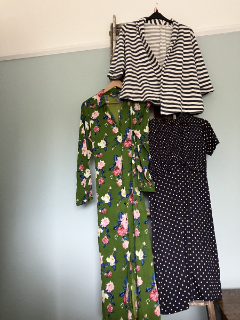 Three items of clothing on hangers: a green floral dress, a black and white dotted dress and a navy and white-striped jacket