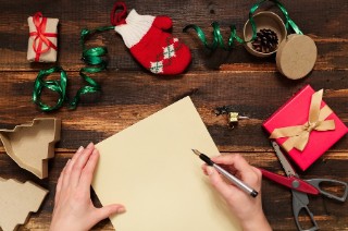 A blank piece of paper, a hand holding a pen, and Christmas decorations scattered around