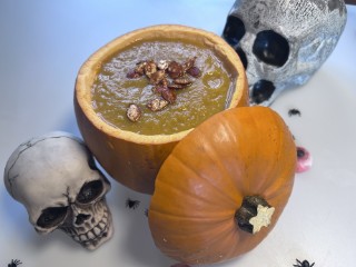 A pumpkin hollowed out and filled with soup. Two fake skulls and plastic spiders surround it.
