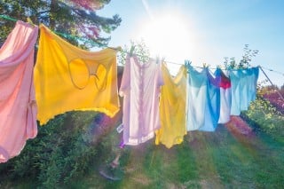 Yellow, pink and blue clothing hanging on an outdoor line, with the sun shining through them