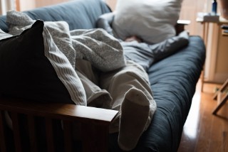 Man lies on sofa with cushions on top of him