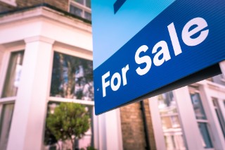 A blue 'For sale' sign outside a house