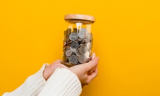 Caucasian hands holding a jar of coins against a yellow background