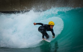 A child surfing, wearing a black wetsuit