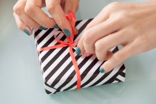 A pair of hands unwrapping a gift, which is wrapped in black and white striped paper