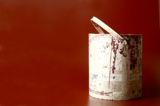 An old, dirty paint tin against a maroon background