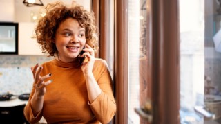 Smiling young woman on a mobile phone, looking out of a window.