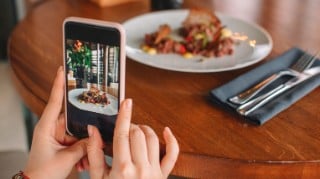 Close up of a young woman taking a photo of a meal on a table with a smartphone.