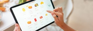 Woman shopping food online using a digital tablet at the kitchen, close-up view on a tablet screen. Concept of buying online using mobile devices